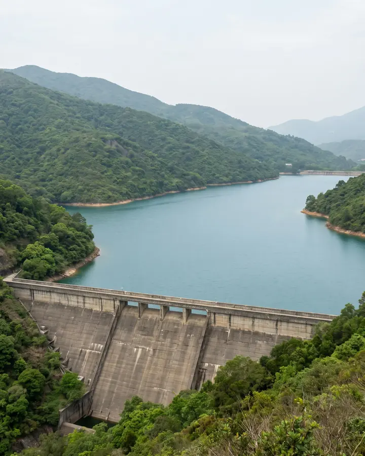 An ordinary concrete dam holding back a full reservoir between forested hills.